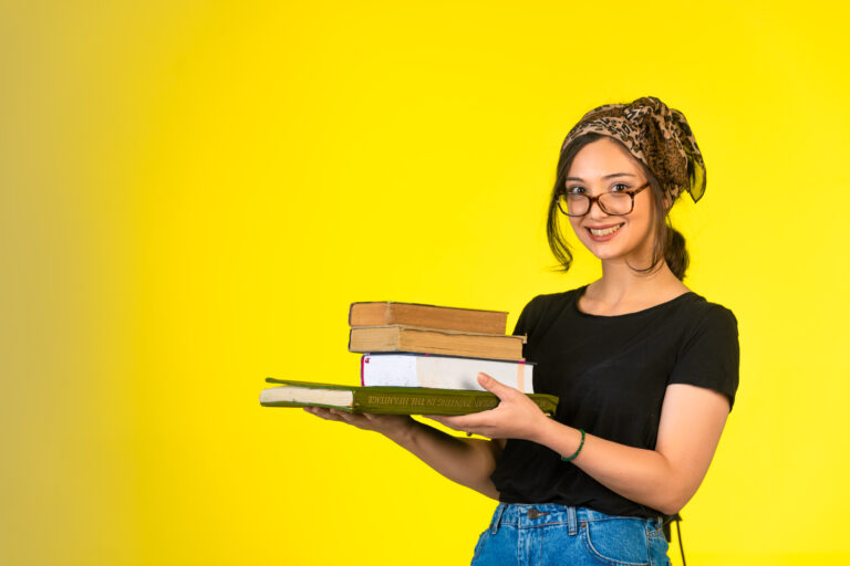 Young schoolgirl in eyeglasses holding her books and positively smiling
